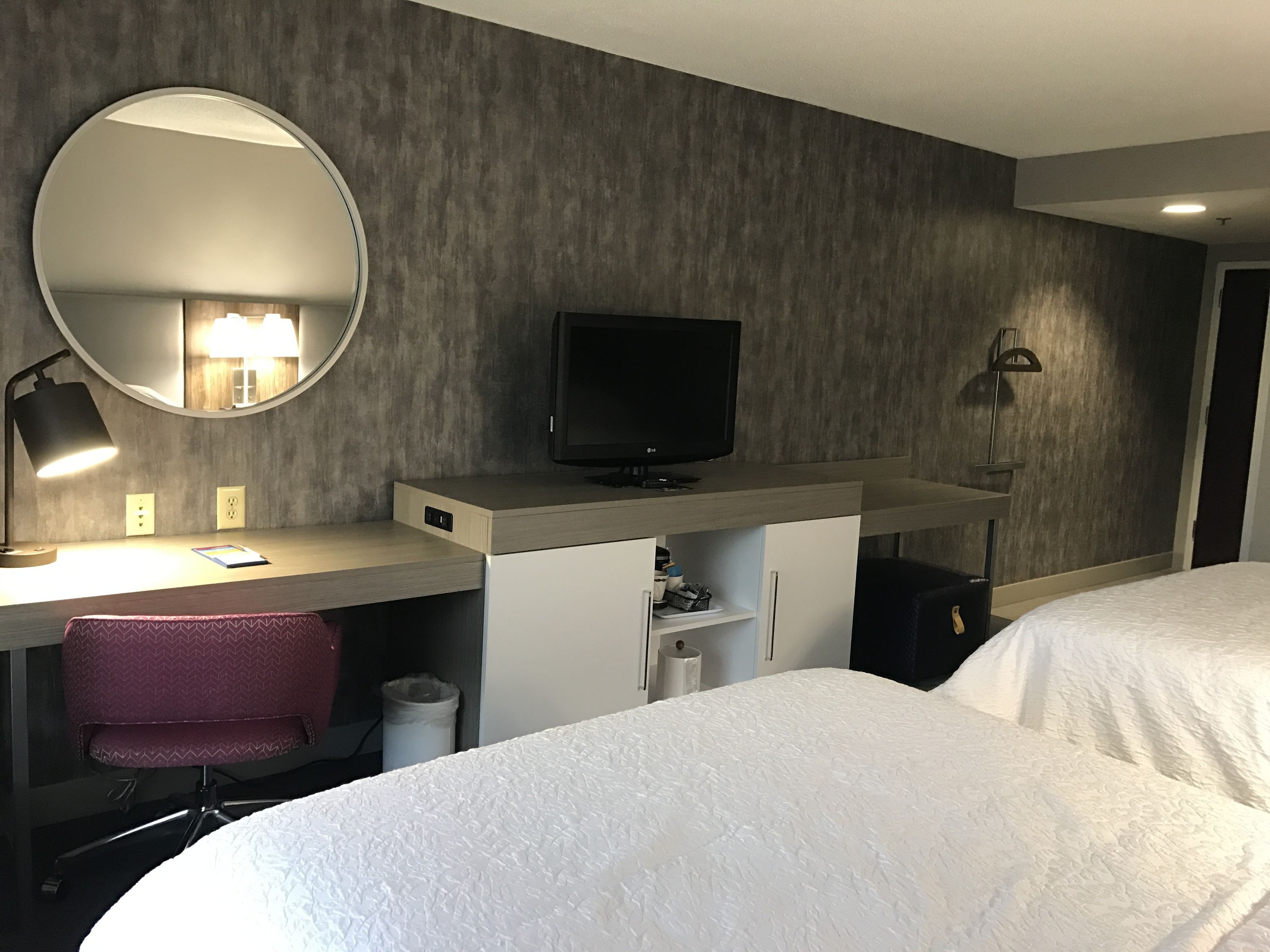 Une chambre d’hôtel équipée d’un bureau, d’une télévision, d’un miroir et de deux lits.