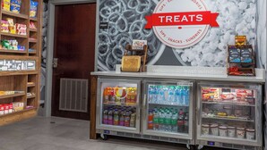 A snack and sundries section with a 'Treats' sign, a beverage cooler stocked with various drinks, and shelves with snacks and sundries. - Hampton Inn East Windsor (Hightstown)