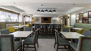 A modern dining area with high tables and chairs, a central decorative wall, and a view of the outdoors. - Hampton Inn East Windsor (Hightstown)