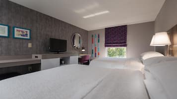A hotel room with two beds, a desk, a television, a mirror, and a window with curtains.