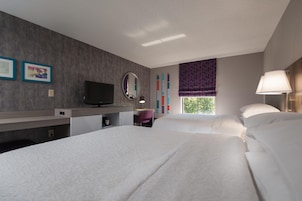 Habitación de hotel con dos camas, un escritorio, televisor, espejo y ventana con cortinas.