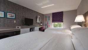 A hotel room with two beds, a desk with a computer, a TV, a mirror, and a window with a view of trees. - Hampton Inn East Windsor (Hightstown)