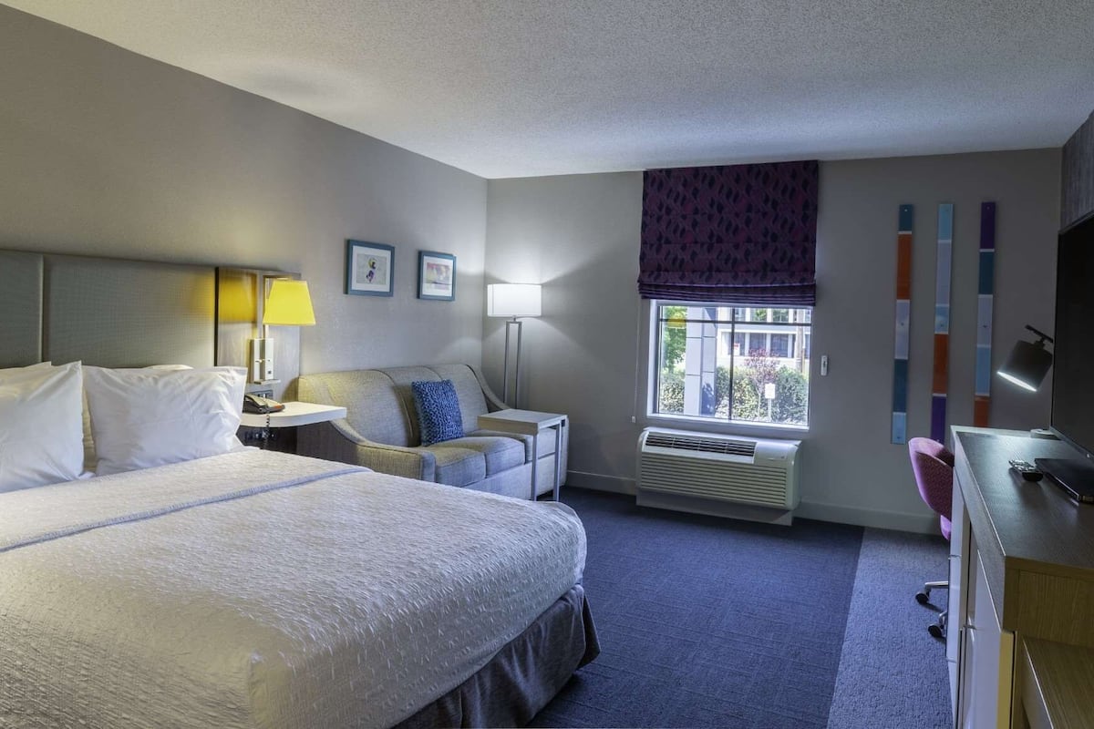 A hotel room with a large bed, a desk with a chair, a window with a view, and a flat-screen TV.