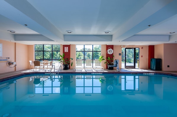 Une piscine intérieure avec des parois en verre transparent, un panneau indiquant qu’il est interdit de plonger, et une vue sur les arbres à l’extérieur.