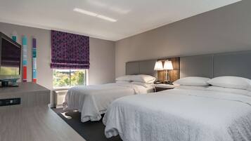 A hotel room with two beds, a desk, a lamp, and a window with a view.
