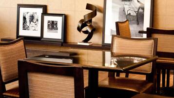 A dining area with a glass table, wooden chairs, a television mounted on a shelf, and framed pictures on the wall.