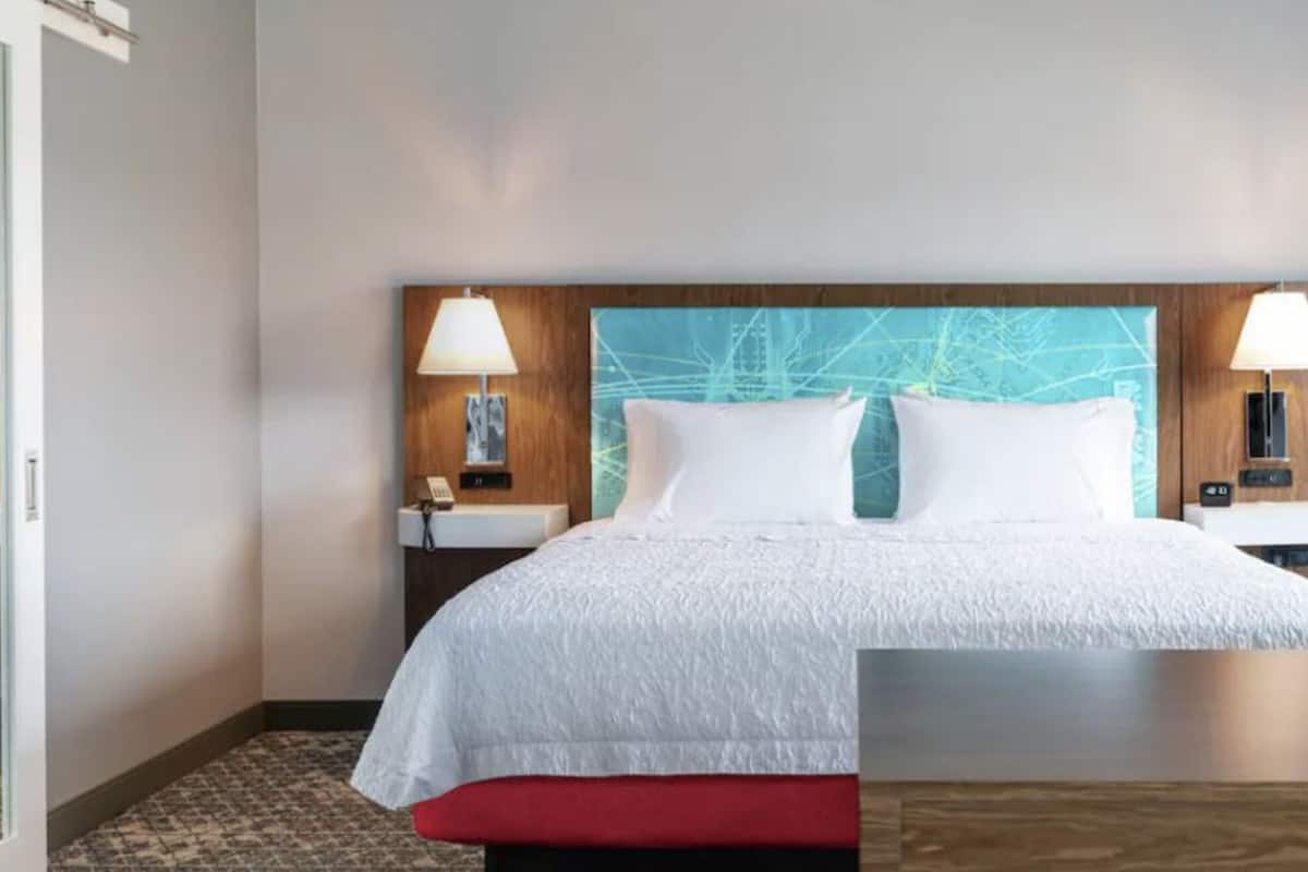 Habitación de hotel con una cama grande, dos lámparas de noche, un cabecero de madera y una ventana con vistas.