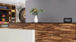 A hotel reception area with a wooden reception desk, a large wall clock, and a floral arrangement.