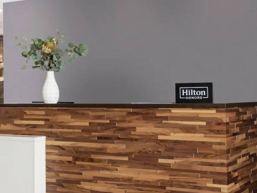 A hotel reception area with a wooden reception desk, a large wall clock, and a floral arrangement.