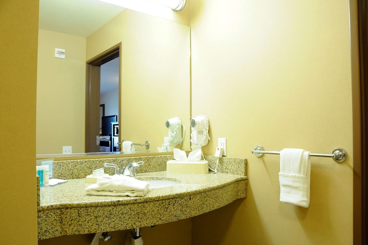 Un baño de hotel con lavamanos de encimera de granito, un espejo y un perchero para toallas.