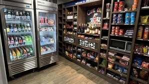 A well-lit convenience store with refrigerated beverage dispensers, snack shelves, and a variety of packaged goods.
