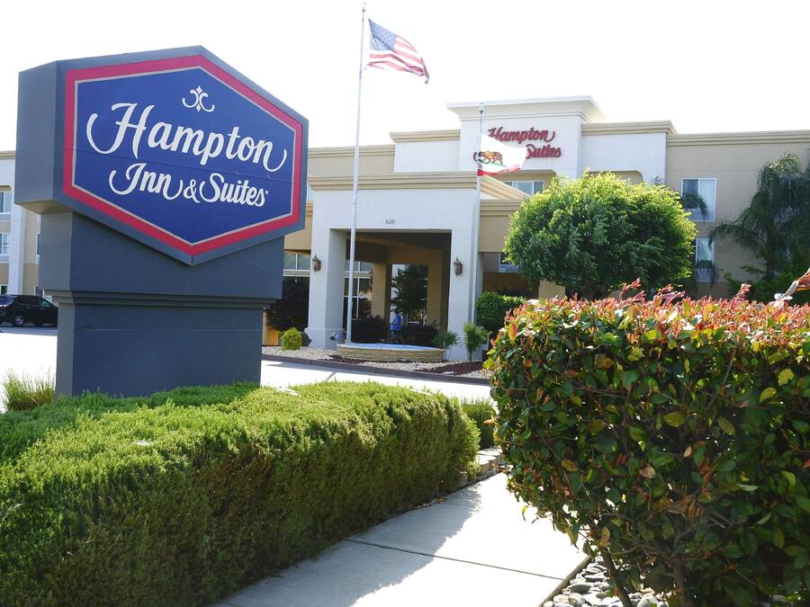 A Hampton Inn & Suites sign and building facade with a flag, surrounded by well-maintained landscaping.