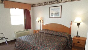 A hotel room with a bed, two bedside tables with lamps, a heater, a window with curtains, and a framed picture on the wall. - Scottish Inn Ronks (Ronks)