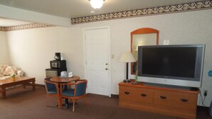 A hotel room with a television on a wooden dresser, a small table with chairs, a sofa, and a coffee maker. - Scottish Inn Ronks (Ronks)