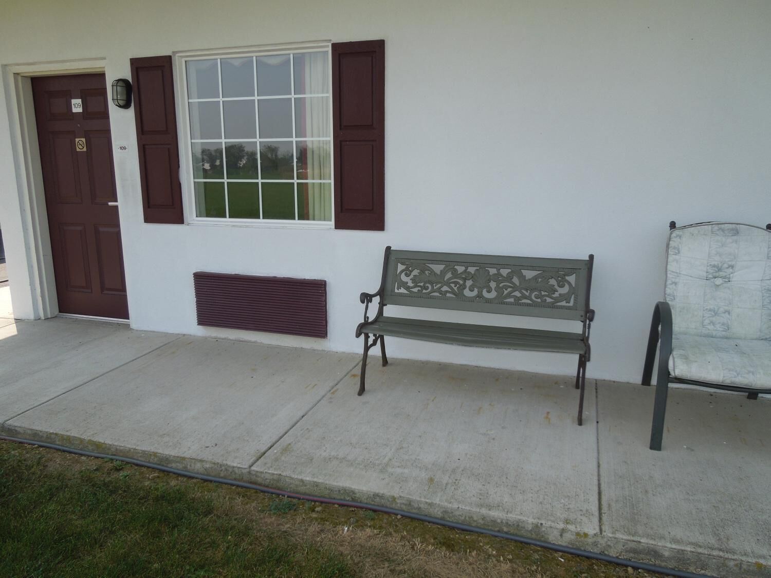 A bench outside a building with a door marked '109', a window with brown shutters, and a vent below the window.