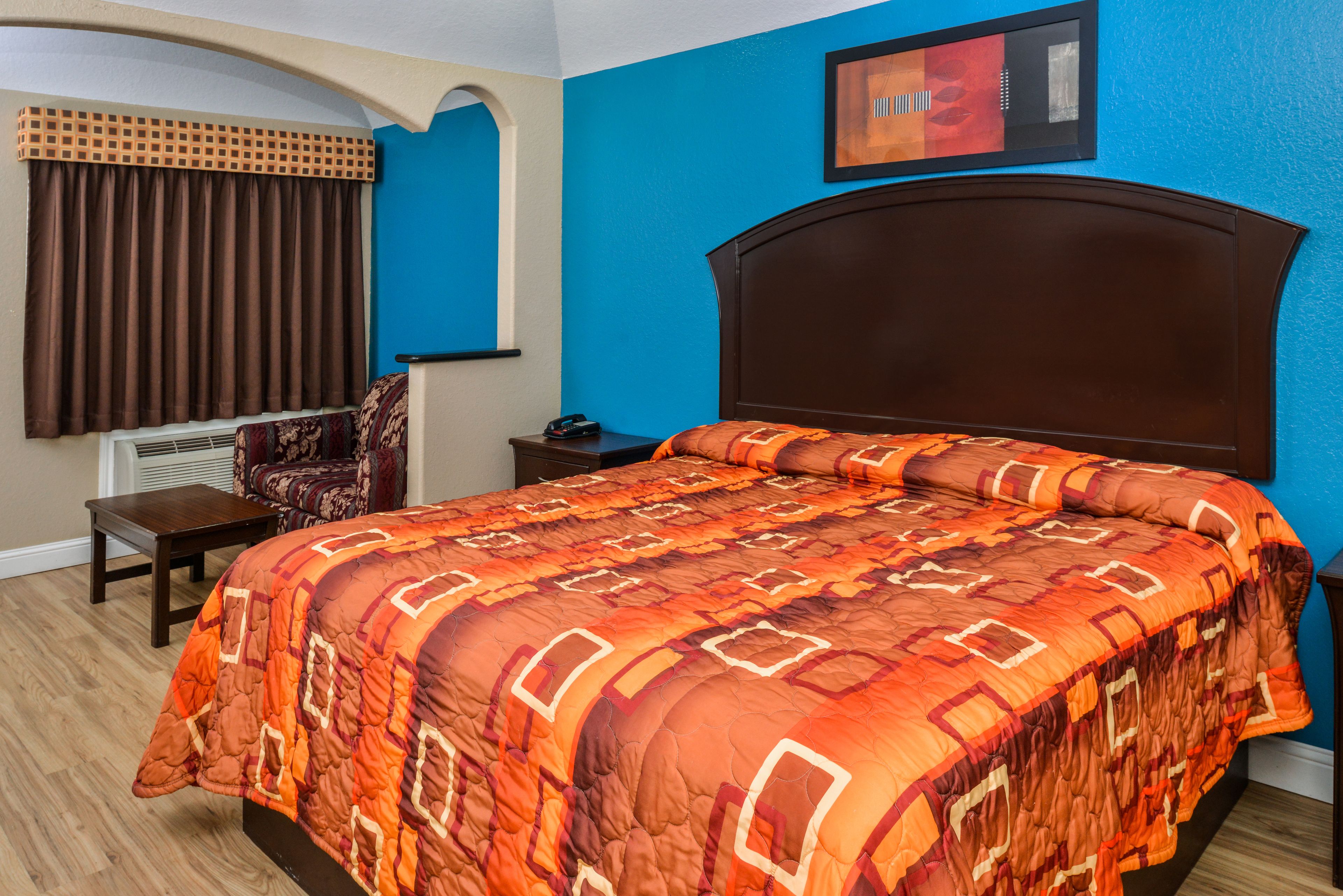 A bedroom with a large bed, a chair, a nightstand, and a window with curtains.
