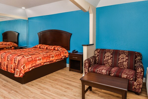 A bedroom with a large bed, a sofa, a nightstand, and a wooden table.
