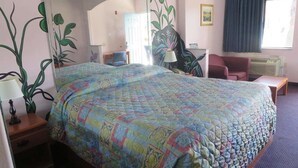 A hotel room with a large bed, a desk, a chair, a lamp, and a window with curtains. - Travelers Inn and Suites Liberty (Liberty)