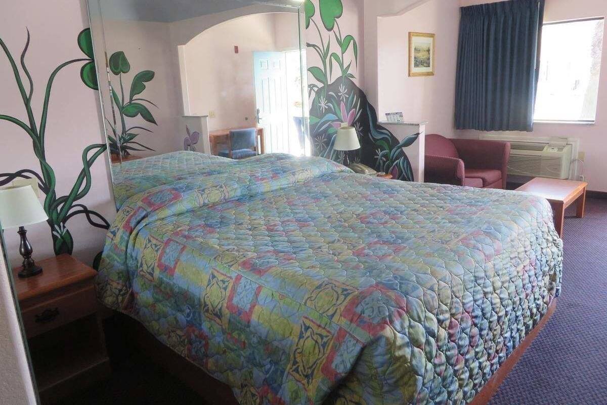 Une chambre d’hôtel avec un grand lit, un bureau, une chaise, une lampe et une fenêtre avec des rideaux.