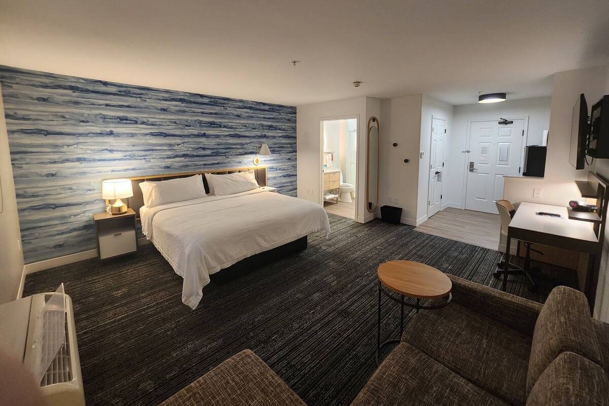 Ein Hotelzimmer mit Bett, Nachttischen, Schreibtisch, Stuhl und einem kleinen runden Tisch.