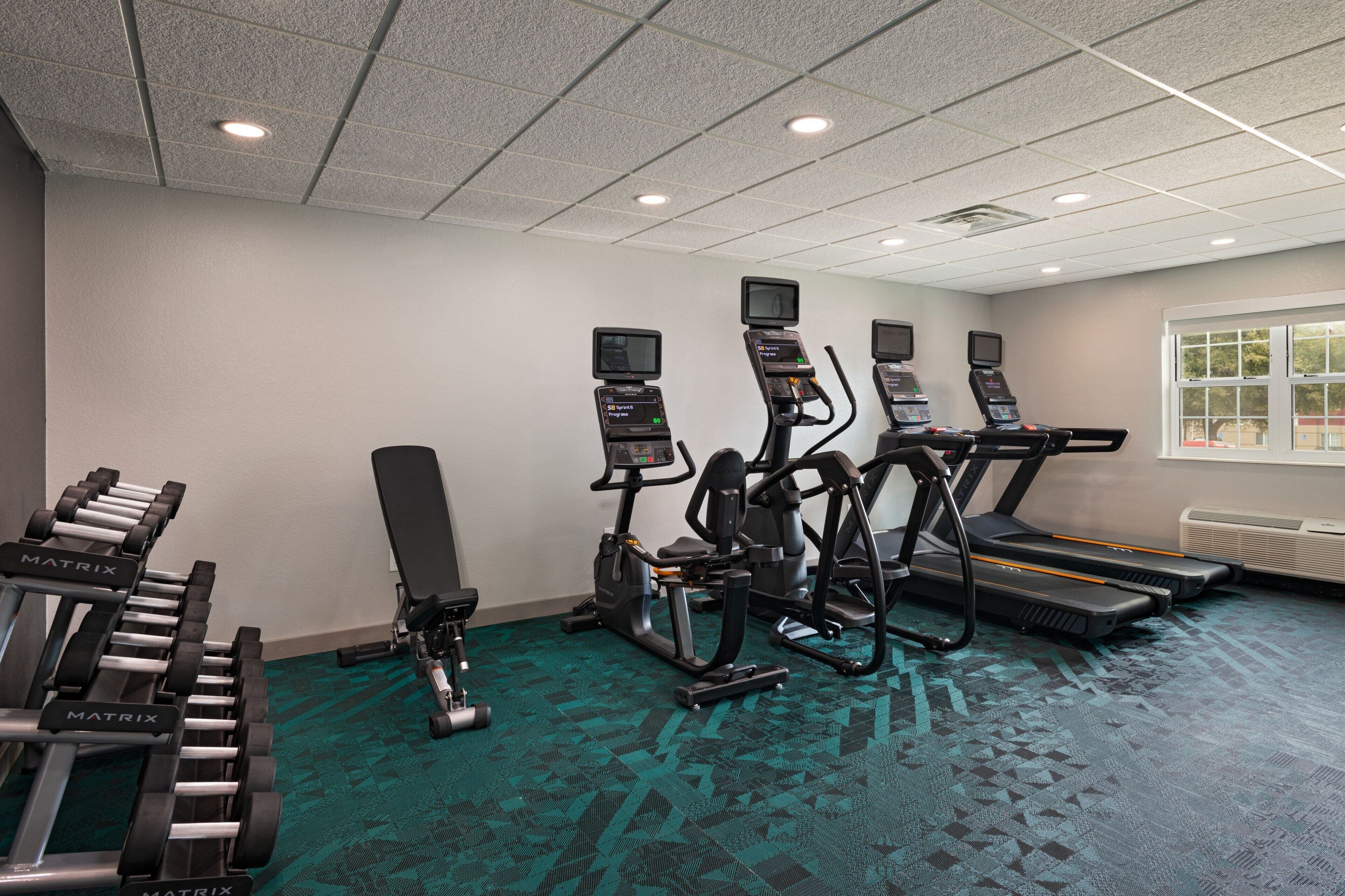 A gym with treadmills, elliptical machines, and dumbbells.