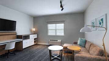 A modern room with a desk, a sofa, a small round table, a standing lamp, and a large window.