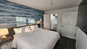 Habitación de hotel con una cama grande, una mesita de noche, una lámpara, una pared con un diseño abstracto azul y un armario con puertas blancas.