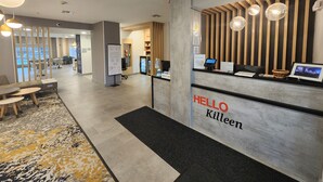 Zona de recepción de un hotel con un letrero que dice 'HELLO Killeen', un mostrador de recepción, un área de estar con mesas y sillas, y vista al comedor.