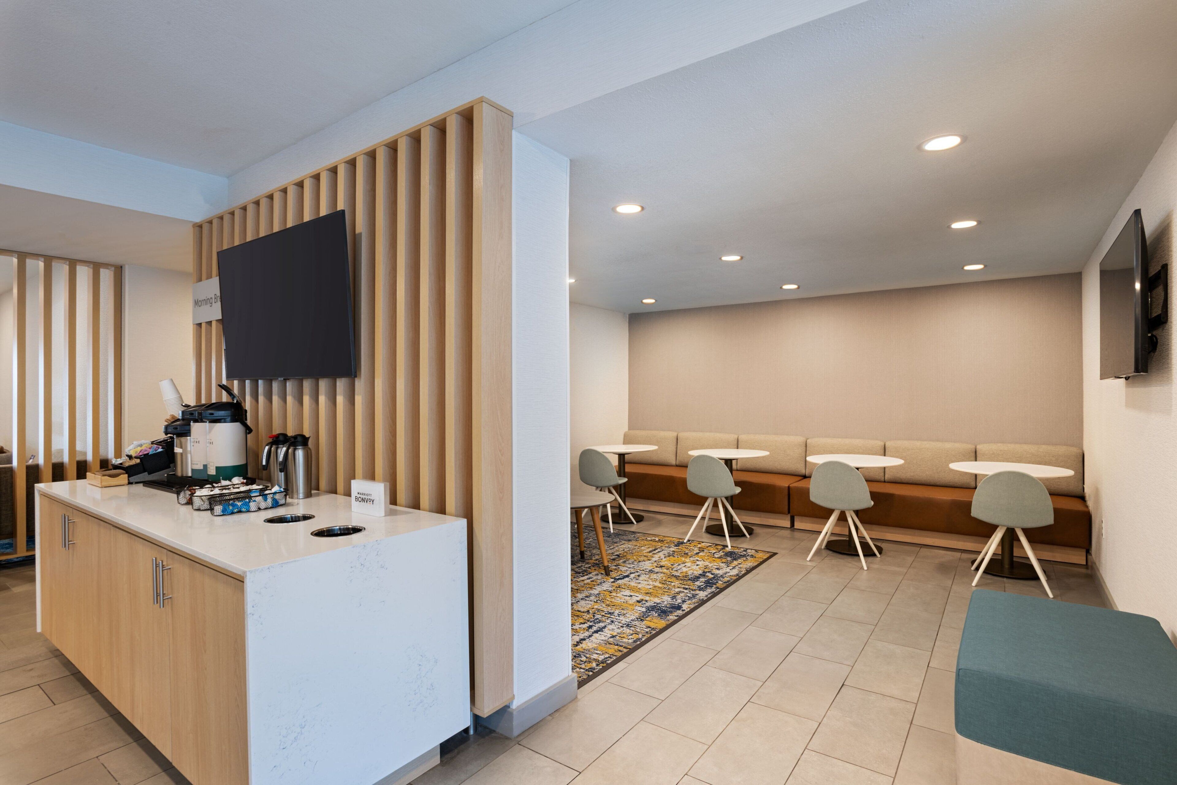 A modern hotel lobby with a reception desk, seating area, and a flat-screen TV mounted on the wall.