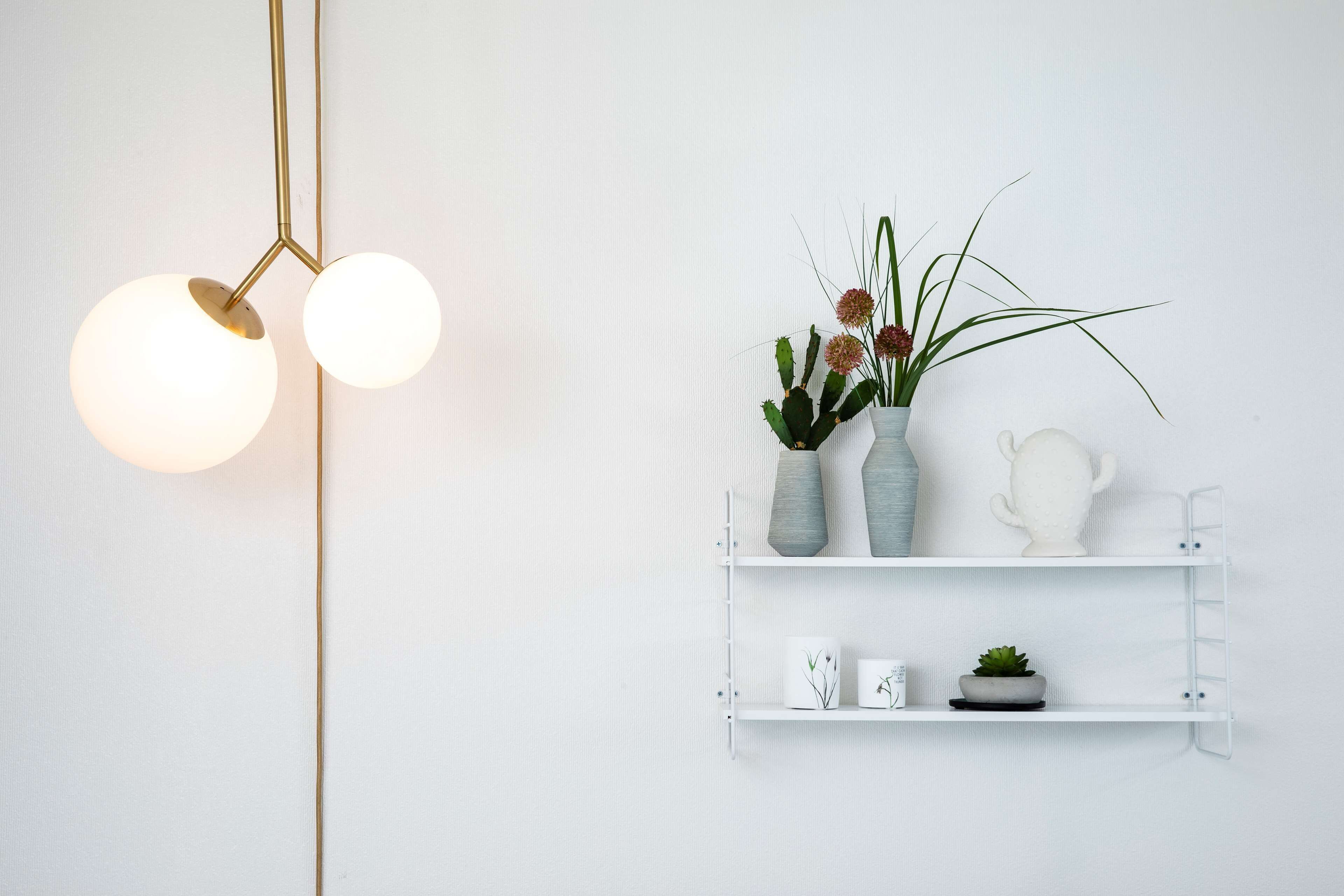 A minimalist wall decor with a white shelf holding vases, a teapot, and a small plant.
