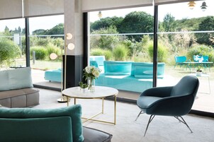 Un interior moderno con sofás color turquesa, una mesa redonda y vistas a un jardín exuberante a través de ventanas amplias.
