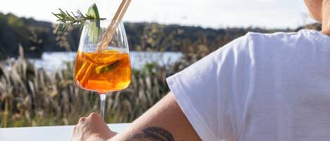 A person holding a glass with a drink garnished with a slice of lime and a sprig of rosemary.