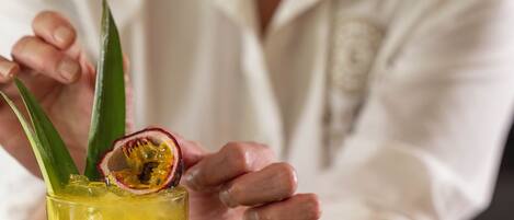 A person holding a cocktail glass with a passion fruit and lime garnish, with limes and a passion fruit on the table.