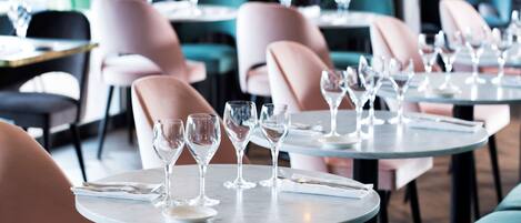 Interior de un restaurante con mesas redondas, sillas y copas de vino dispuestas para comer.
