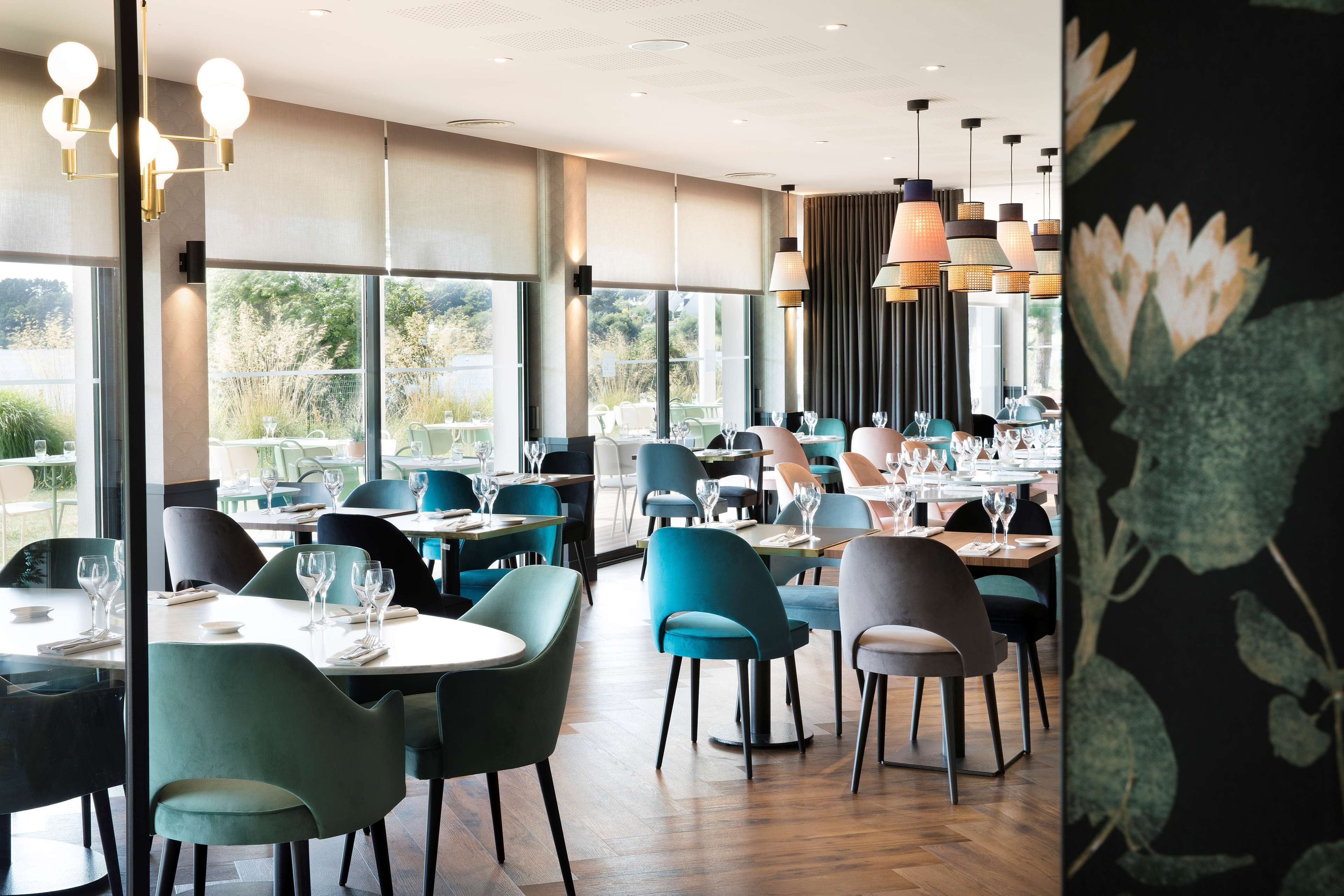Un restaurante con varias mesas y sillas, amplios ventanales y lámparas colgantes.