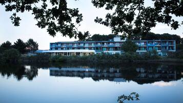 A multi-story hotel with a modern design, located near a body of water, featuring balconies and large windows.