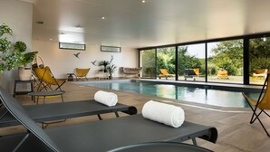 A modern indoor swimming pool area with lounge chairs, a small table, and potted plants. - Best Western Plus Hotel Les Rives Du Ter (Larmor-Plage)