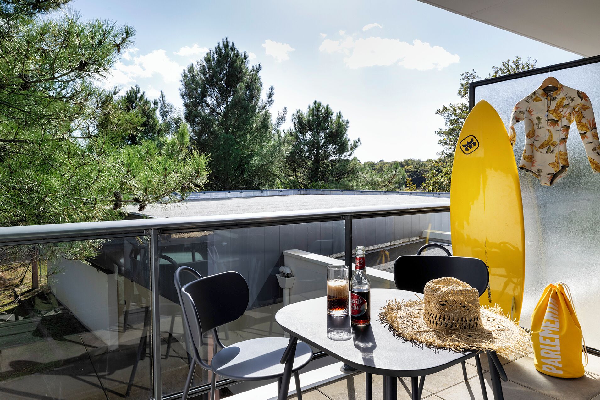 Un balcon avec une table, des chaises, une planche de surf et une bouteille de bière.
