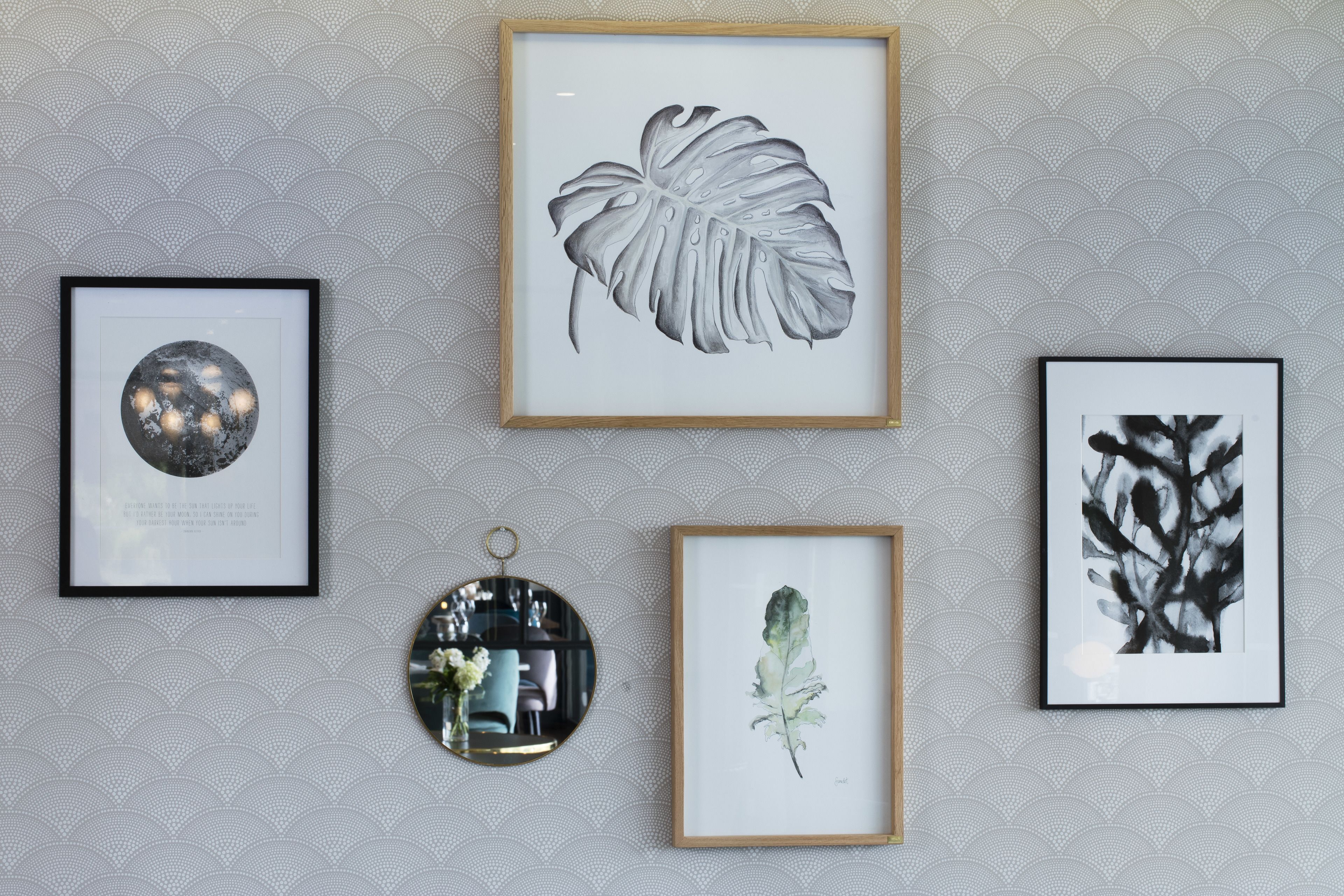A wall with four framed artworks: a leaf, a flower, a globe, and a black and white abstract piece.