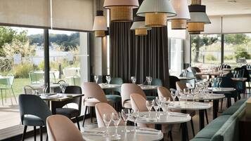 A restaurant with round tables and chairs, large windows, and hanging pendant lights.