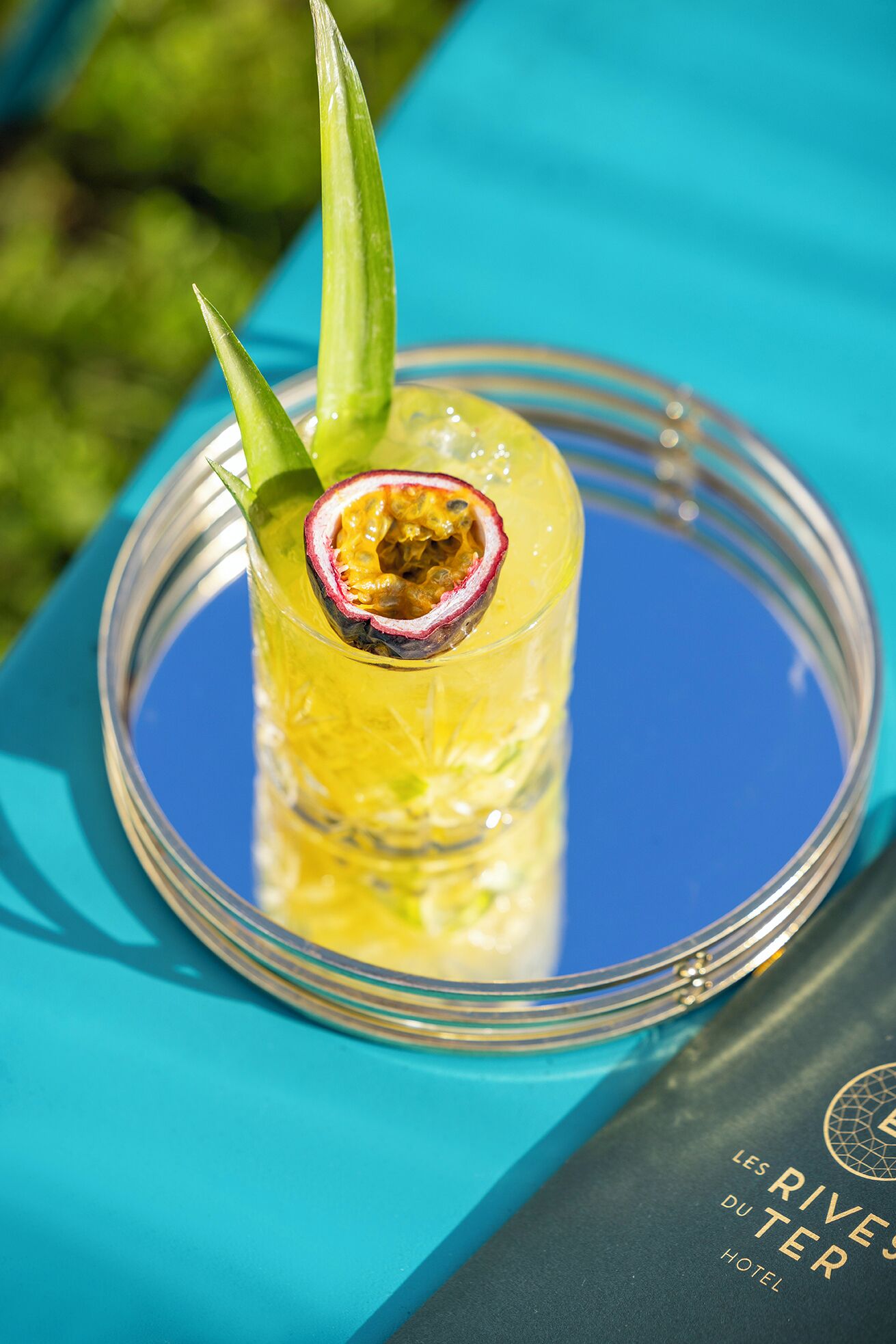 Un vaso de bebida amarilla adornado con una fruta de la pasión sobre una mesa azul.