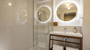 Un baño moderno con ducha envuelta en vidrio, tocador de madera con espejo y lavamanos blanco.