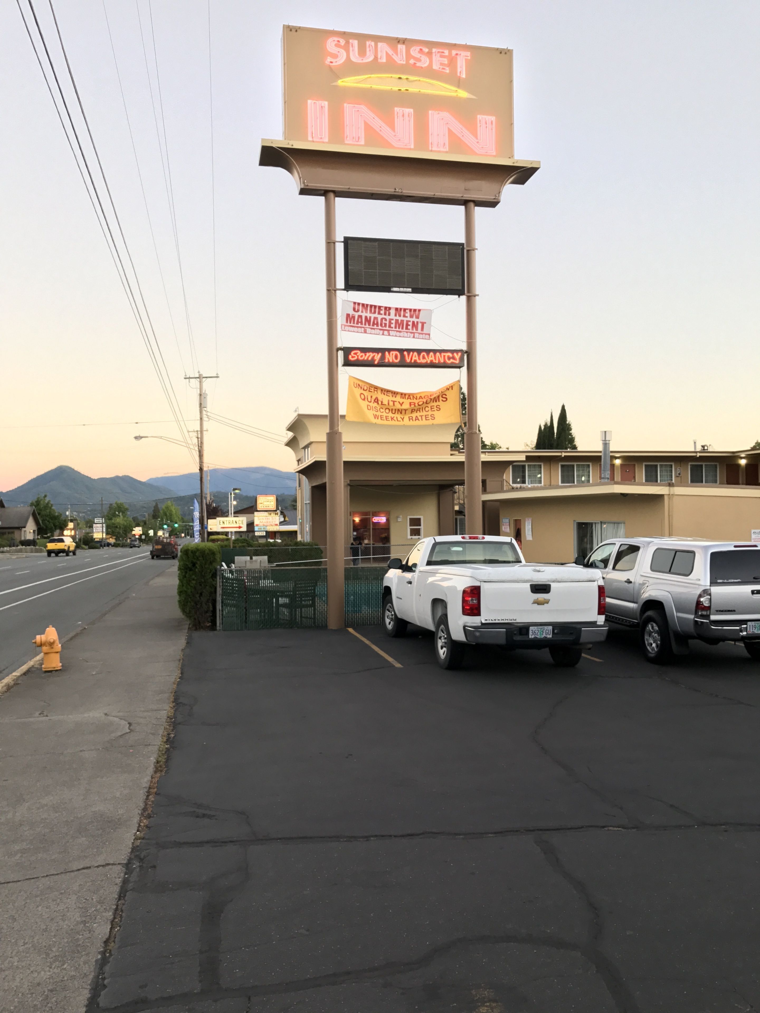 Un motel appelé « Sunset Inn », avec une enseigne au néon, un parking où sont garés plusieurs camions et un poteau d’incendie sur le trottoir.