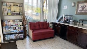 Eine Hottelobby mit einem roten Sofa, einer Pinwand mit verschiedenen Mitteilungen, einer Küchenzeile mit einem Toaster und einem gerahmten Bild an der Wand.