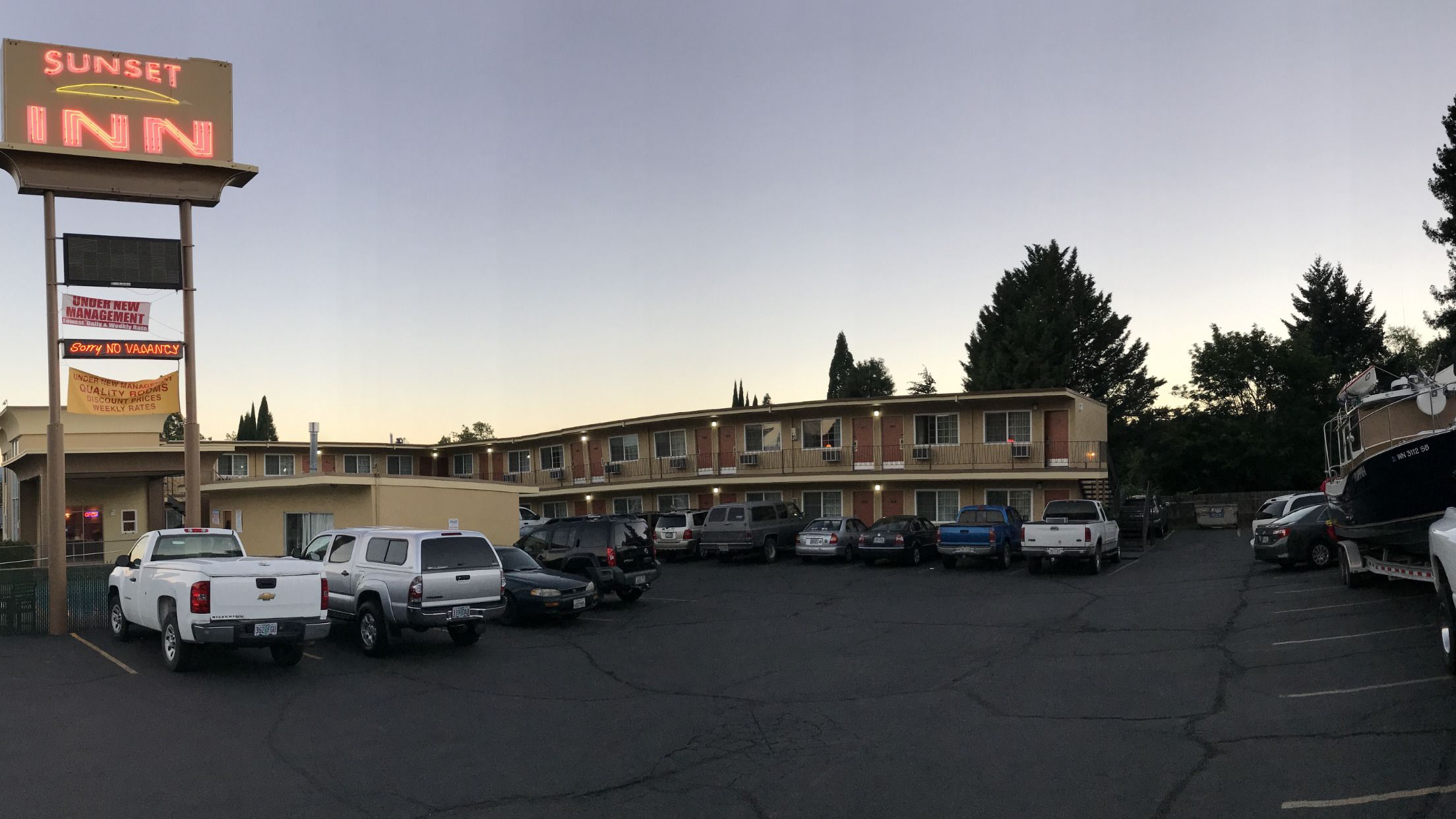 Pousada Sunset com um estacionamento cheio de carros, um edifício de vários andares e uma placa indicando 'Sem quarto disponível'.