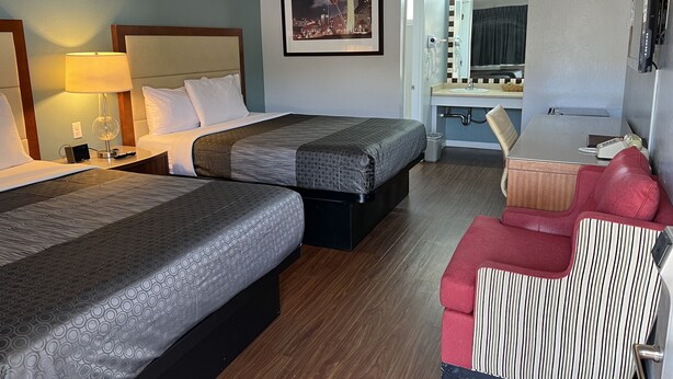 Ein Hotelzimmer mit zwei Betten, einem Schreibtisch, einem Sessel, einem Schminktisch mit Spiegel und einem gerahmten Bild an der Wand.