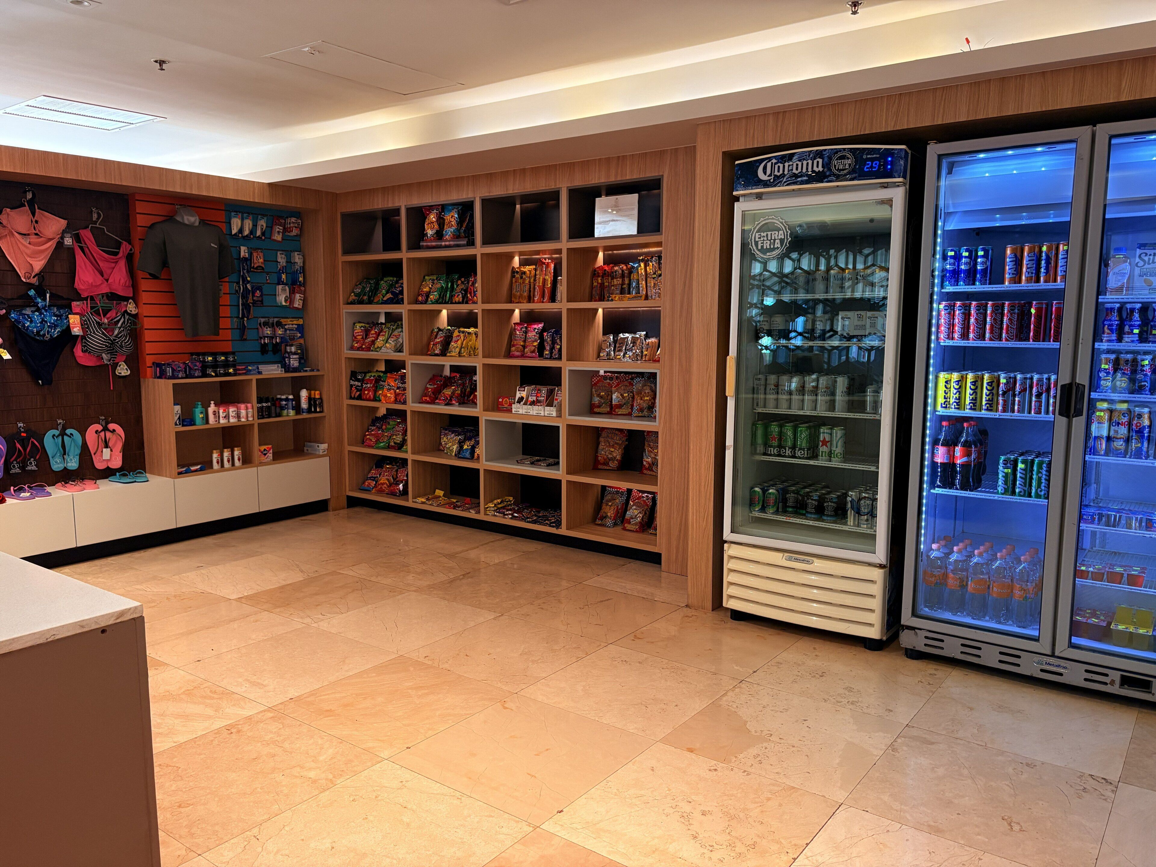 A store with shelves stocked with snacks, a refrigerated display case with beverages, and a section with hanging items.