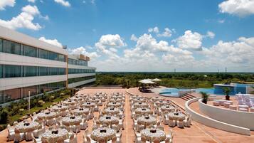 A rooftop terrace with round tables and chairs, a pool, and a view of the landscape.