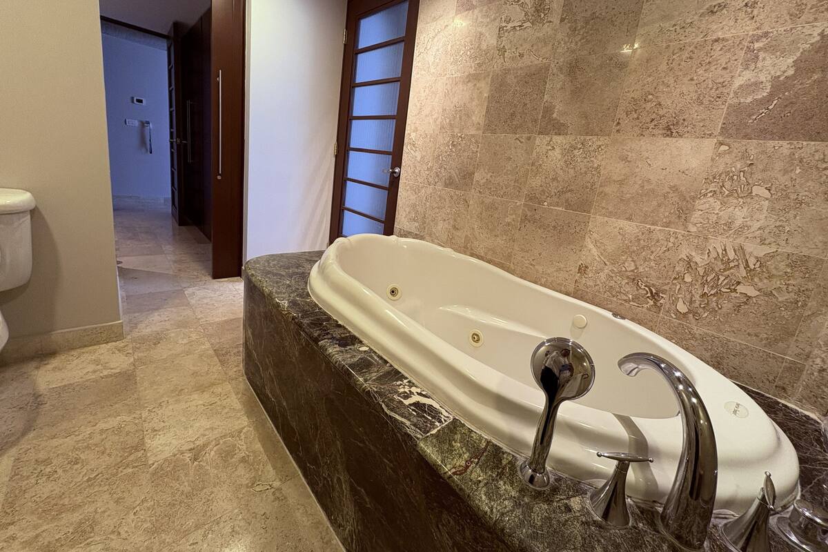 A bathroom with a marble bathtub, a toilet, and a shower area.
