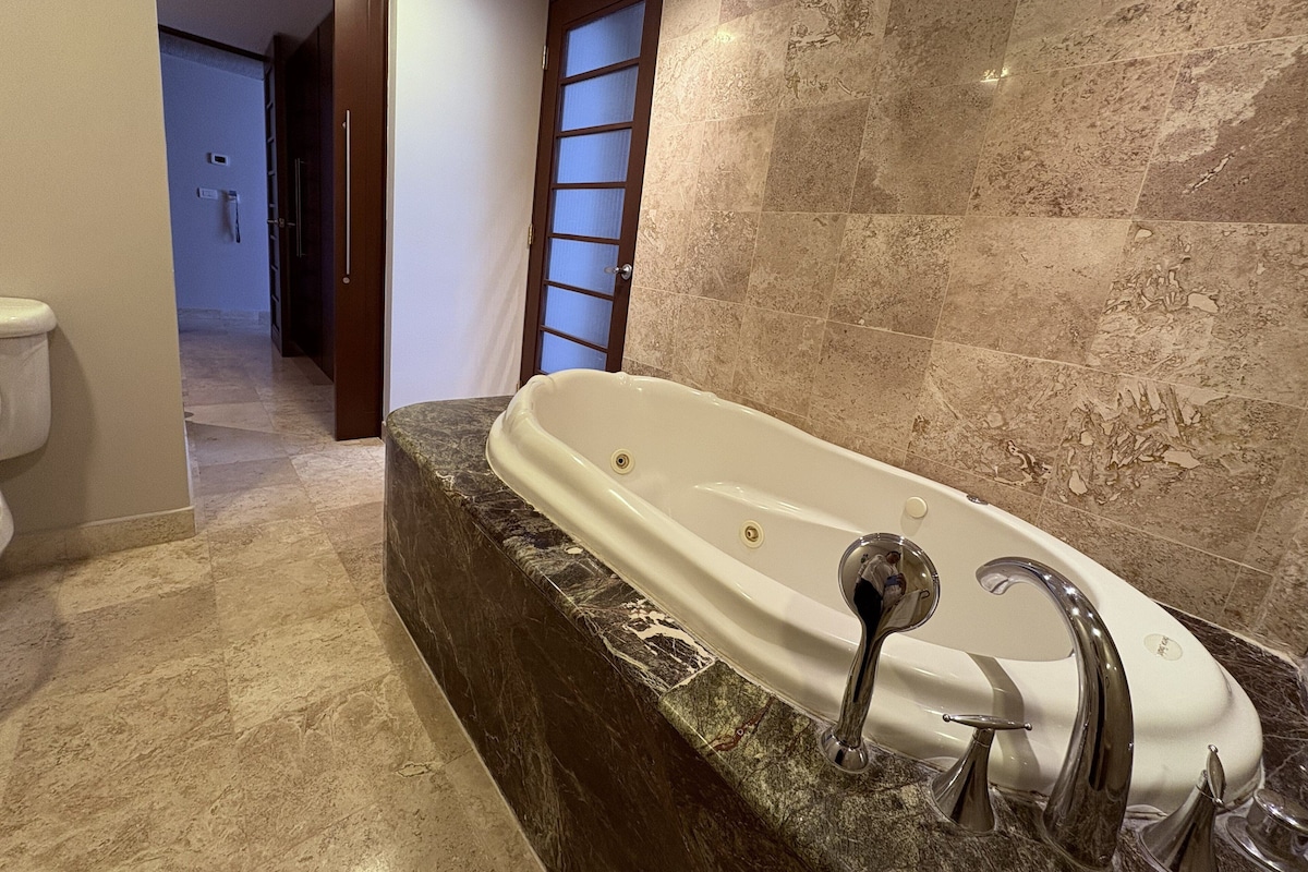 Un baño con bañera de mármol, inodoro y zona de ducha.